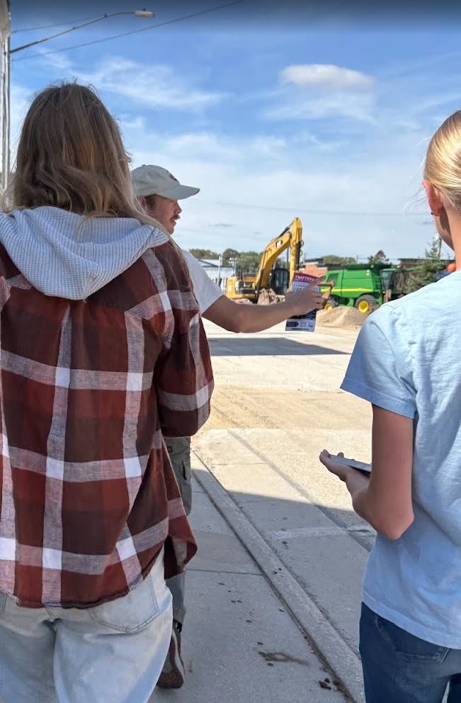 Three Save Wisconsin Saturday volunteers stand near a construction area with Tom Tiffany campaign literature.