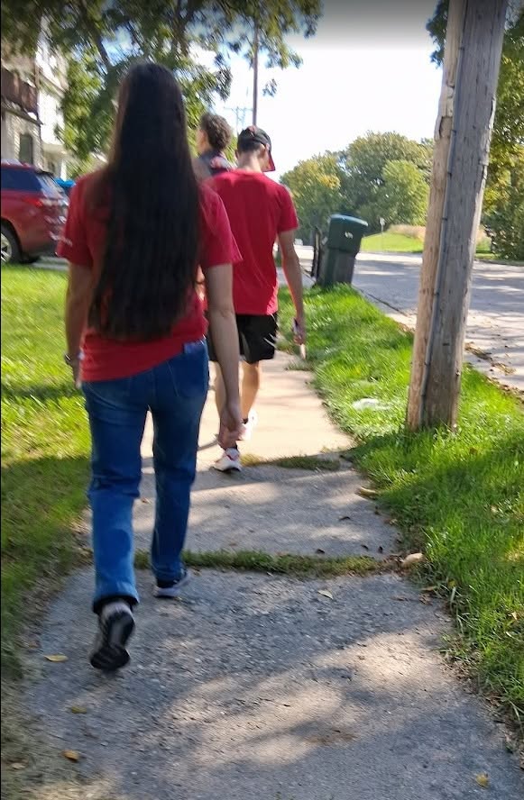 Three volunteers walk down a residential sidewalk carrying campaign literature.